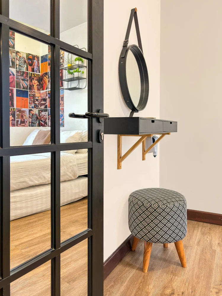 Brooklyn: Rak rias dengan cermin bulat dan stool, di balik pintu kaca berbingkai hitam.