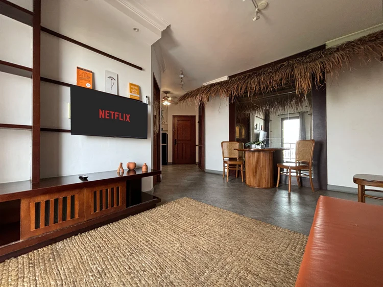 Ubud: Smart TV dengan Netflix di rak kayu, karpet anyaman menutupi lantai ruang tamu.