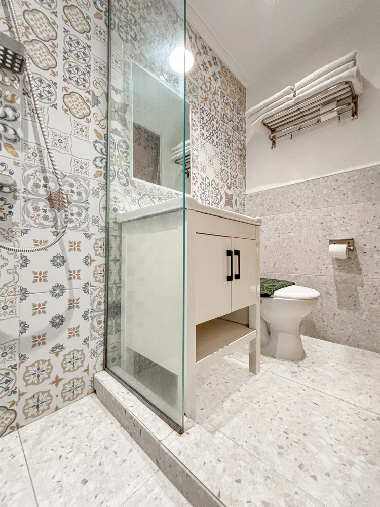 St. Tropez: Kamar mandi modern dengan ubin bermotif, shower berdinding kaca, dan meja wastafel.
