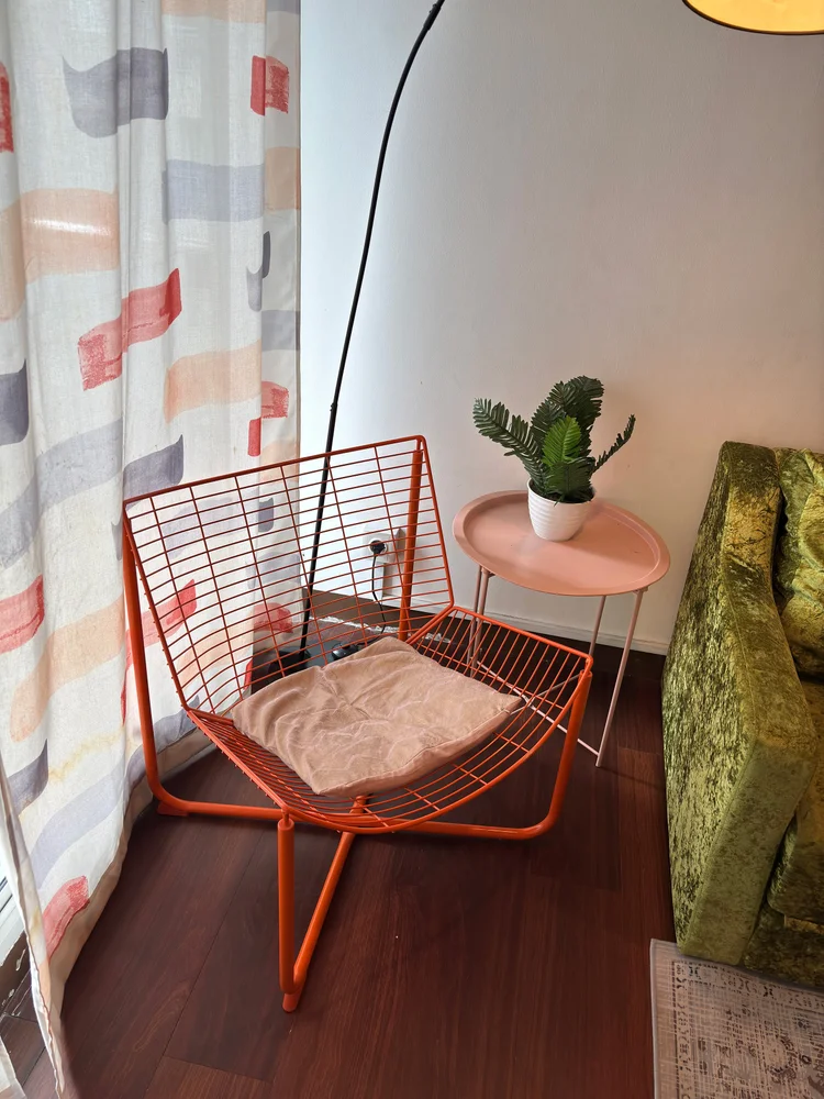 Namibia: Kursi kawat oranye dengan meja kecil, sudut santai di samping sofa.