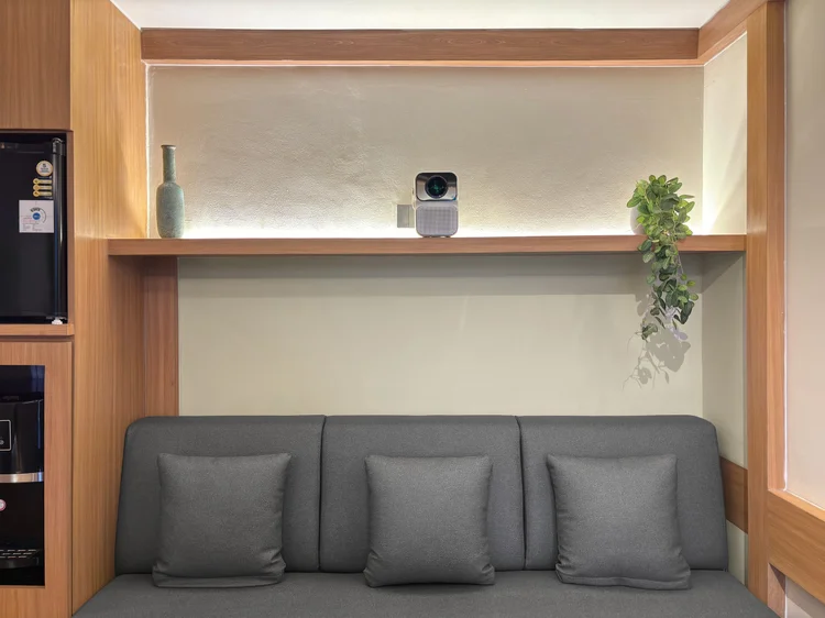 Kawaguchi: Sofa tiga dudukan menghadap layar, proyektor pintar ada di rak atas.