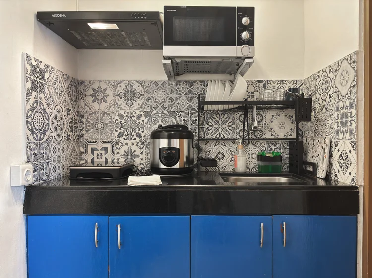 Santorini: Dapur terbuka dengan lemari biru: kompor induksi, microwave, rice cooker, dan alat masak dasar.