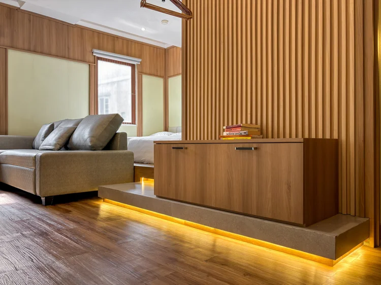 Sapporo: Sofa di atas panggung kayu dengan lampu di bawahnya, sekat kayu ke area tidur.