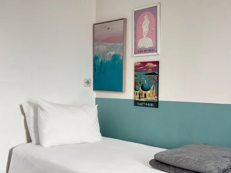 Santorini: Kamar dengan single bed, dinding hijau toska, dan poster bertema Santorini.