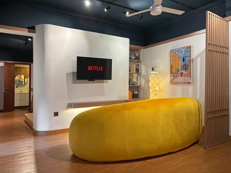 Kyoto: Sofa kuning melengkung menghadap smart TV dengan Netflix, ruang santai yang nyaman.