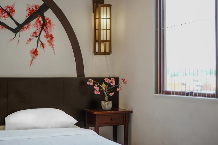 Yokohama: Kamar dengan ranjang tunggal di bawah mural sakura yang sama, AC dan meja nakas kecil.