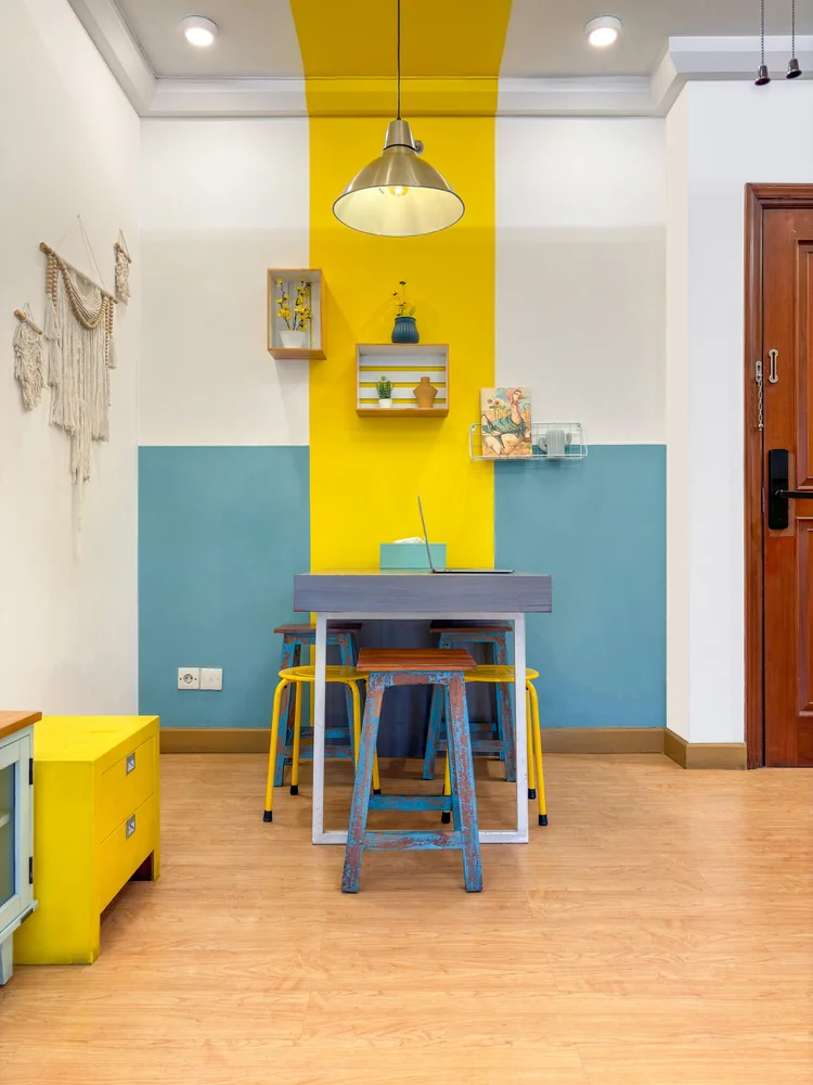 St. Tropez: Meja makan untuk berempat dengan stool warna-warni, di bawah lampu gantung.
