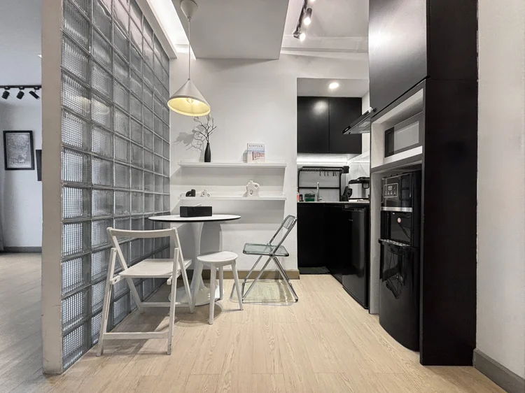 Sydney: Studio bertema Grayscale: dinding glass block, meja makan, dan dapur hitam putih.