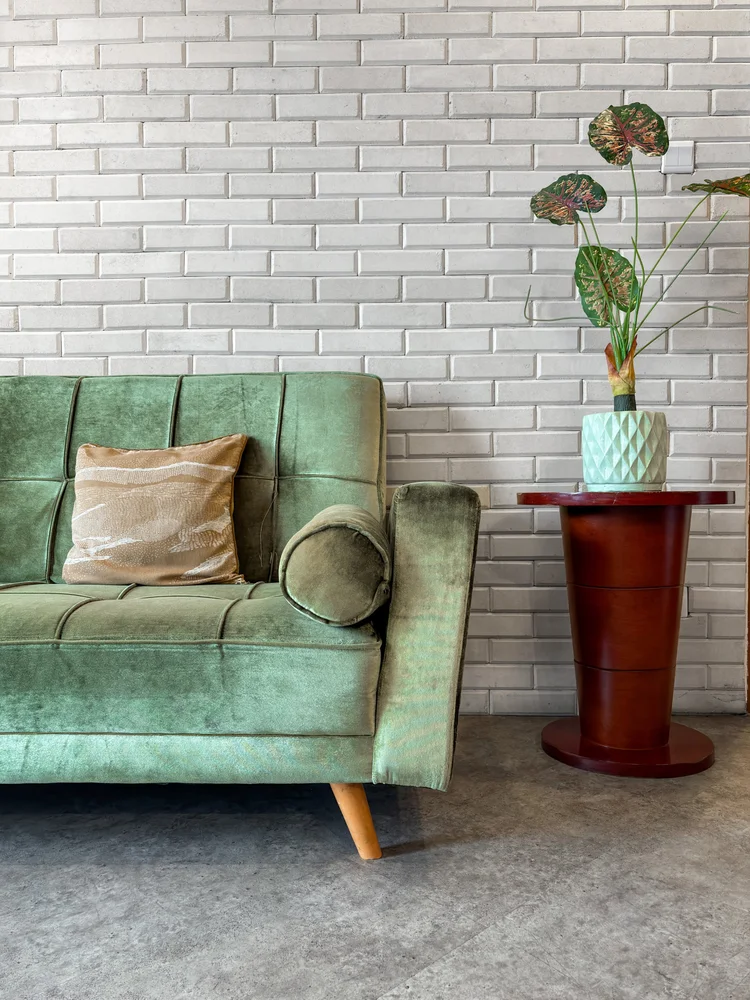 Chicago: Sofa hijau dengan bantal dan meja kecil untuk tanaman, di depan dinding bata putih.
