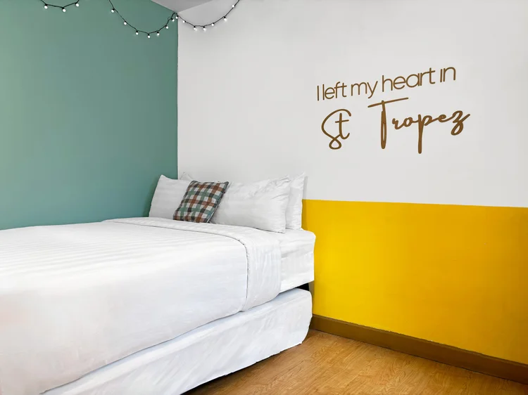 St. Tropez: Area tidur dengan tulisan di dinding dan lampu hias, sprei putih standar semua unit kami.