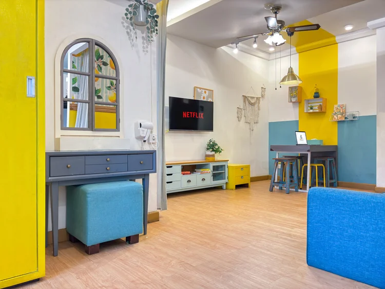 St. Tropez: Studio bertema Summer: aksen kuning dan biru, meja rias di dekat pintu, ruang tamu di ujungnya.