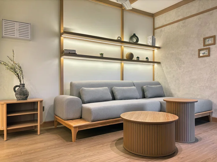 Nara: Ruang keluarga Nara: sofa L Japandi abu-abu, rak dinding, dan meja bundar kayu.