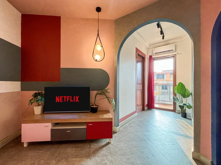 Geneva: Smart TV dengan Netflix di atas konsol merah muda, menghadap sofa oranye.