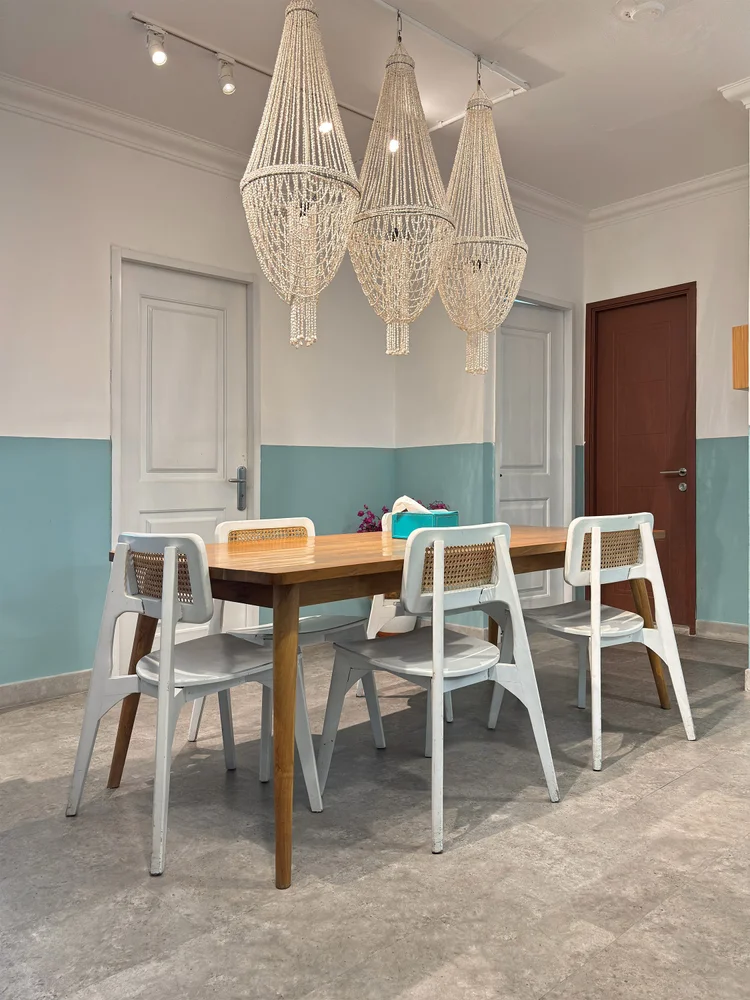 Mykonos: Lampu gantung macrame di atas meja makan, pintu kamar-kamar di sekelilingnya.